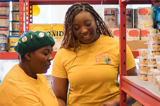 Two grocery market employees conversing beside shelves of canned goods.