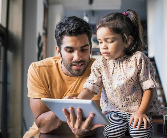 A father shows his young daughter how to use a tablet